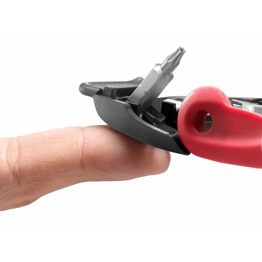 Facom E112PB screwdriver with red handle and interchangeable bit touching a finger, close-up on white background.