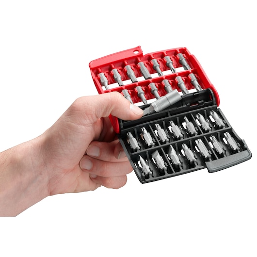 A hand holding an open Facom E120PB compact case containing an assortment of screwdriver bits, neatly organized in red and black plastic compartments.