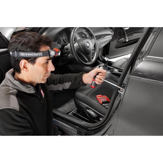 Facom screwdriver set E_120 used by a person for car door repair, red and black handle, bit set on seat.
