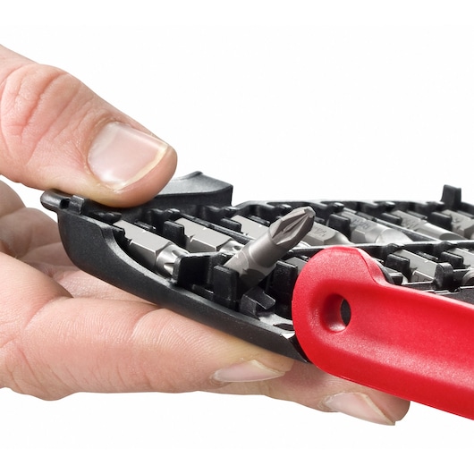Close-up of a hand selecting a screwdriver bit from a black and red Facom bit holder, showing various metal bits arranged in the holder.