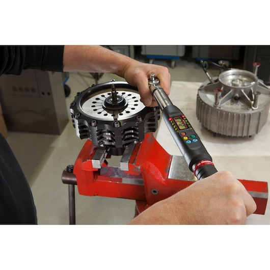 Facom E_306A135S digital torque wrench tightening a mechanical part in a red vise, close-up photo.
