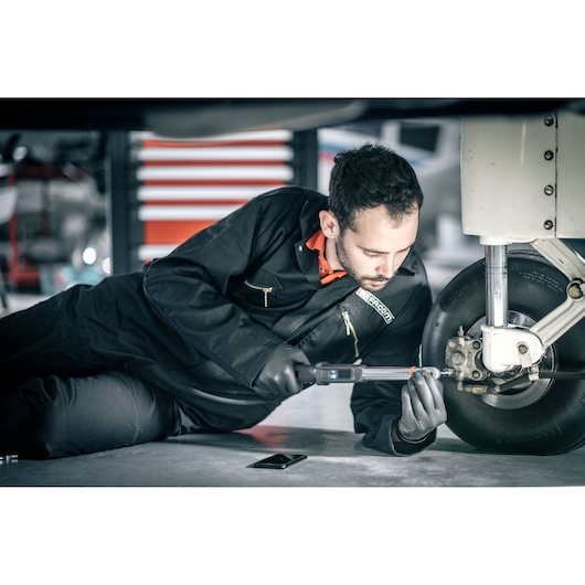 Facom E_516ST-30PB torque wrench used by mechanic on aircraft wheel, workshop setting.