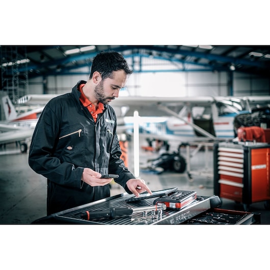 Facom E_516ST-30PB technician using tools near tool chest in airplane hangar, tool tray visible.