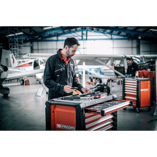 Facom E_516ST-30PB tool chest in hangar, open drawer with tools, technician in foreground, aircraft in background.