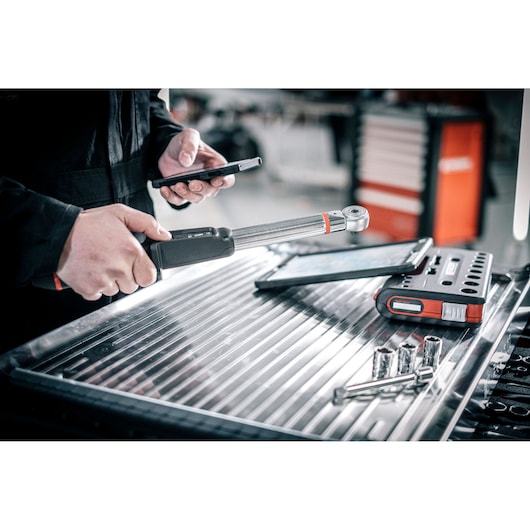 Facom E_516ST-30PB torque wrench in mechanic’s hand with digital tools and sockets on metal workbench