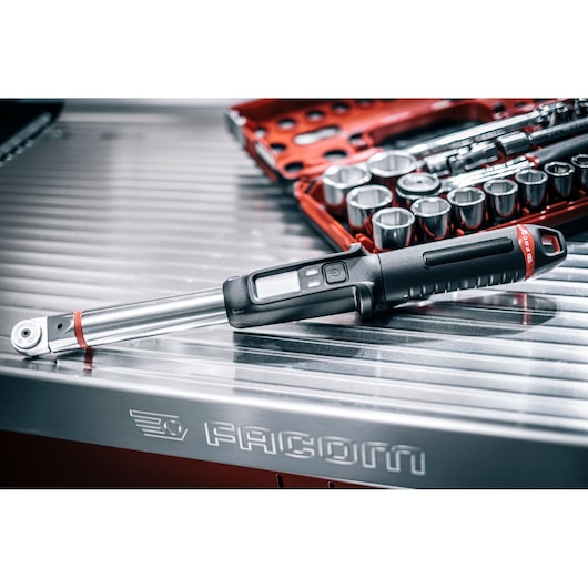 Facom E_516ST-30PB digital torque wrench on metal surface with socket set in background.