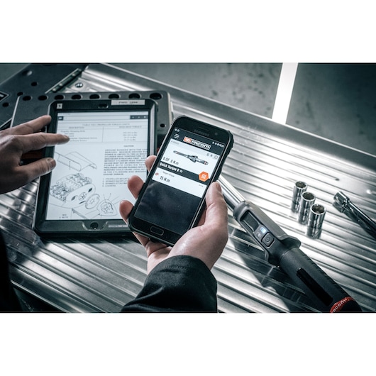 Facom E_516ST-340PB tablet and smartphone used for tool information on metal workbench, digital torque wrench visible.
