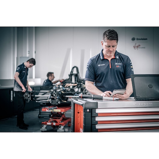 Facom E_516ST-340PB photography of technician at tool cabinet with laptop in workshop, two others working on vehicle.