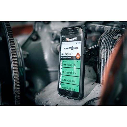 Facom E_516ST-340PB smartphone displaying torque values in industrial engine setting, angled view.