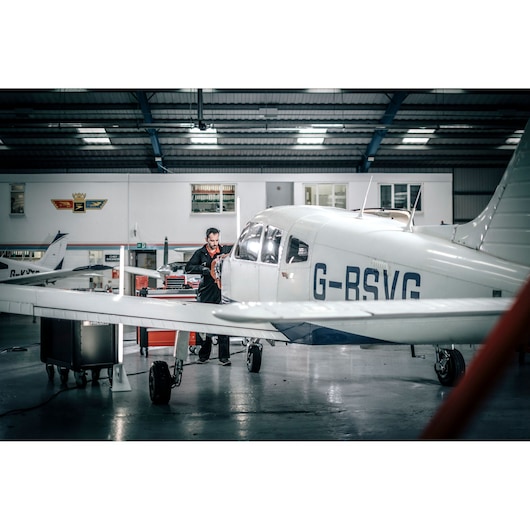 Facom E_516ST-340PB photography of a white small aircraft in a hangar, mechanic with tool cart near nose section.