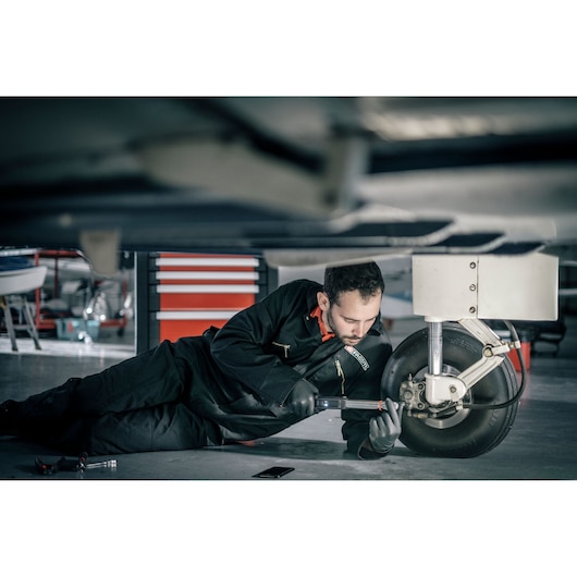 Facom E_516ST-340PB mechanic working on aircraft wheel in workshop, wearing black coveralls.