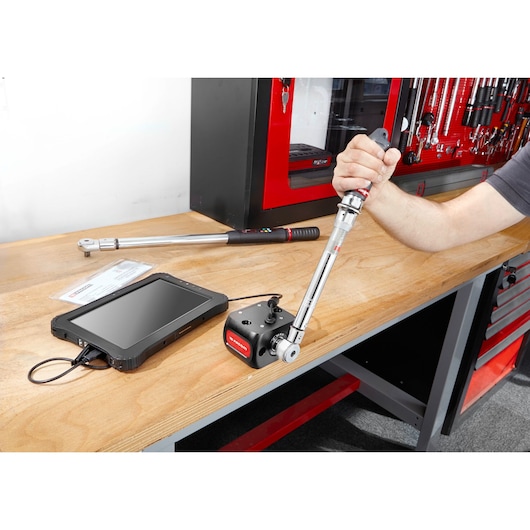 Facom E6000-C50 torque wrench with calibration device and tablet on workshop bench, side angle.