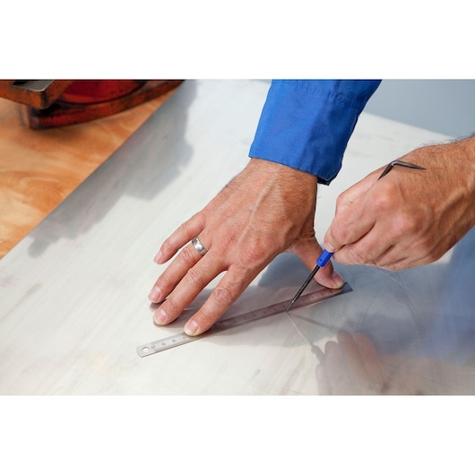 Facom E003601 photography of hands marking metal sheet with ruler and scribe tool.