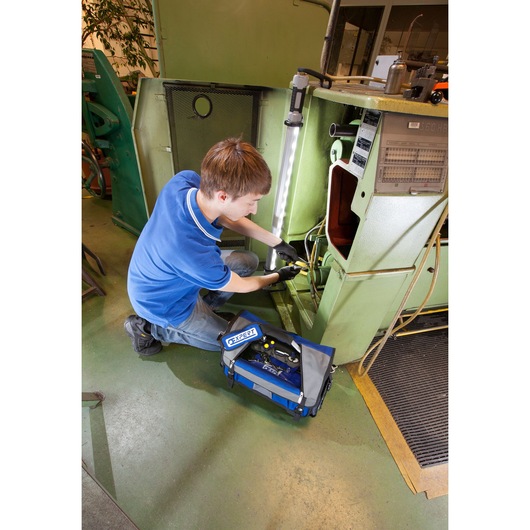 Photo of Facom E010601 blue tool bag on workshop floor beside technician using machine.