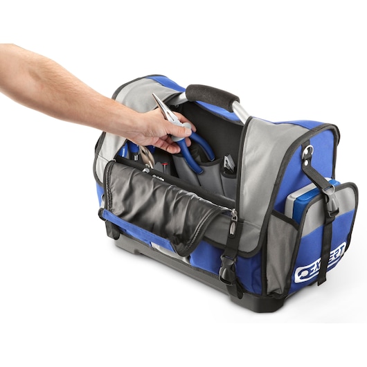 A person is reaching into a blue and grey Facom tool bag filled with various hand tools such as pliers and screwdrivers.