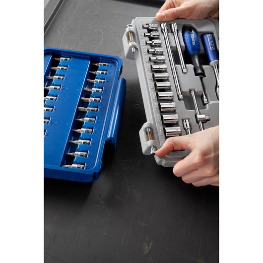 Facom socket set E030702 with blue and gray cases, assorted sockets and tools held by hands on table.