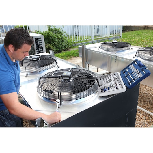 Facom E034805 socket and tool set on outdoor HVAC unit, technician using ratchet wrench, side angle.