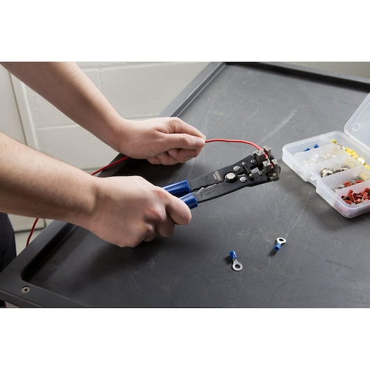 Facom E050105 wire stripper tool with blue handles in use on black surface, connector kit visible.