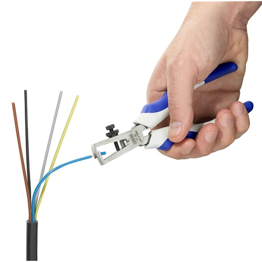 A hand using a Facom wire stripper tool to remove insulation from a blue electrical wire, with other colored wires visible.