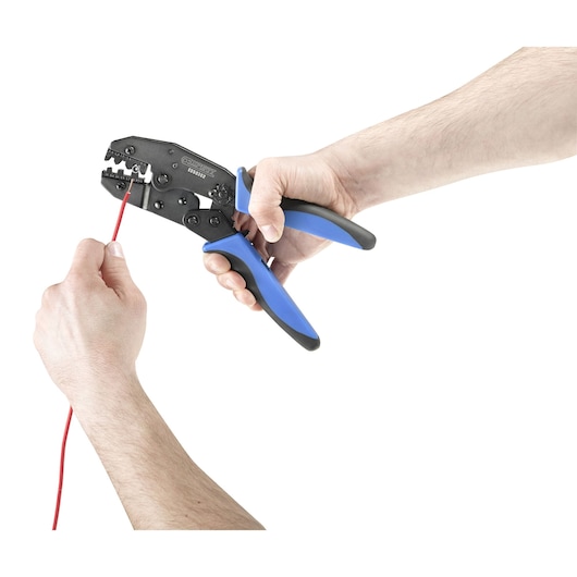A pair of hands using a Facom crimping tool with blue and black handles to crimp a red wire.