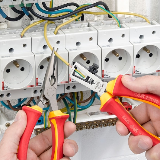 Facom E050416 insulated wire stripping pliers used for electrical wiring near power sockets.
