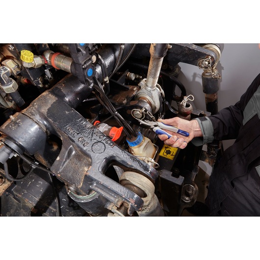 Facom E080505 pliers used for mechanical maintenance, blue-handled tool held by technician near machinery.