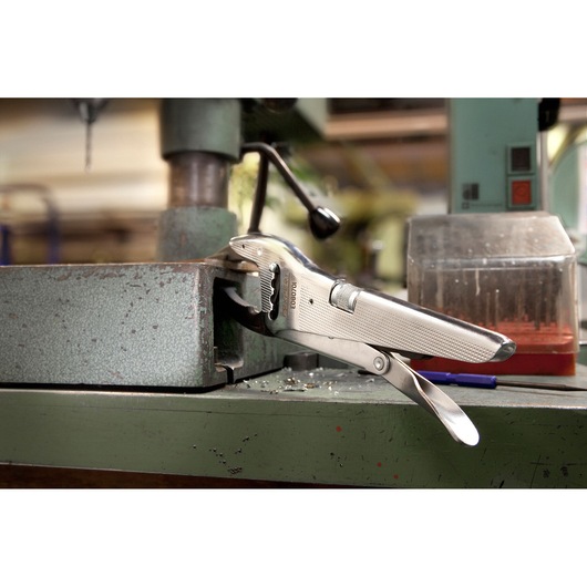 Facom E080701 locking pliers clamping a metal piece on a drill press in a workshop setting.