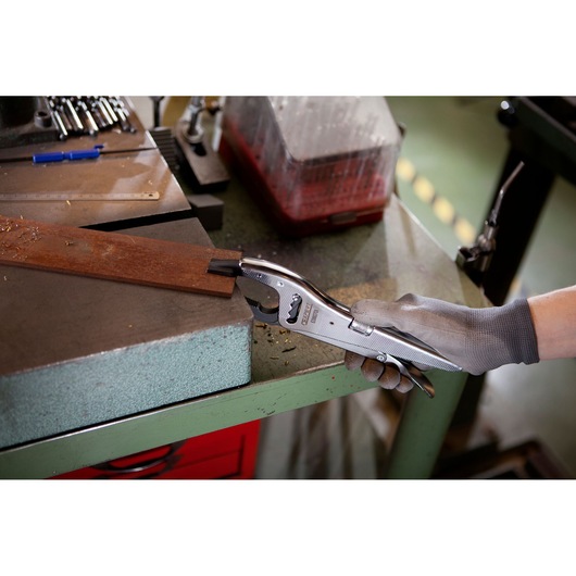 Facom E080701 locking pliers in use on a metal workpiece in a workshop with hand wearing grey glove.