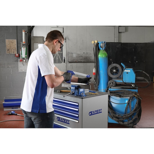 Photo of person using hacksaw with gloves at Facom E090403 tool chest in workshop.
