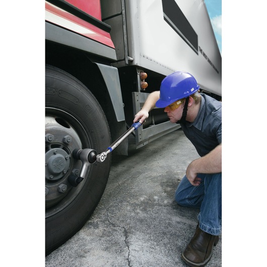 Facom E100106 torque wrench used by a worker tightening truck wheel bolts outdoors.