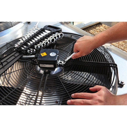 Facom E111102 wrench set used on industrial fan, close-up angle, silver wrenches visible in plastic holder.