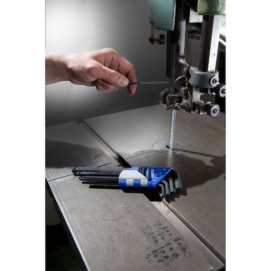 Facom E113976 hex key set in blue holder on metal surface, hand using hex key on industrial machine.