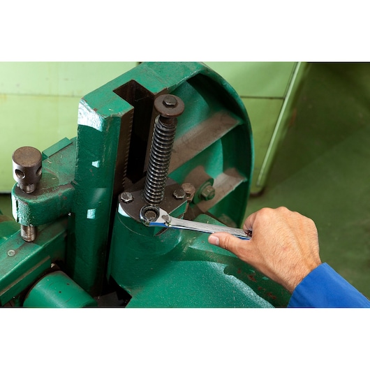 Facom ratcheting wrench E117373 used to tighten a bolt on a green industrial machine, close-up photo.