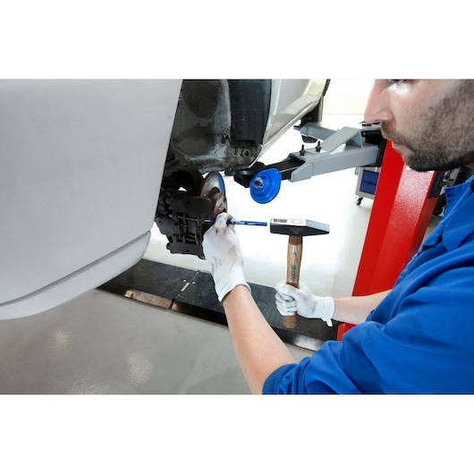 Facom E150102 mechanic using hammer and tool on car wheel hub, photographed from side angle.