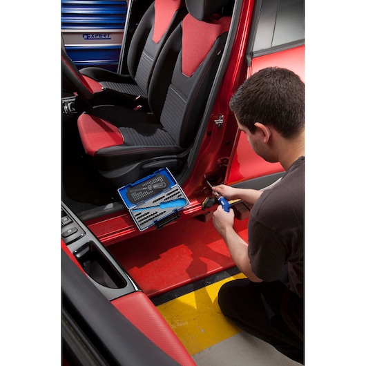 Facom E160804 tool set on car seat during automotive repair, technician using blue tool by door.