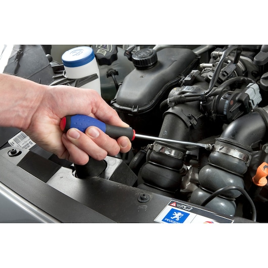 Facom E165138 screwdriver with blue handle used on engine hose clamp, close-up photography.