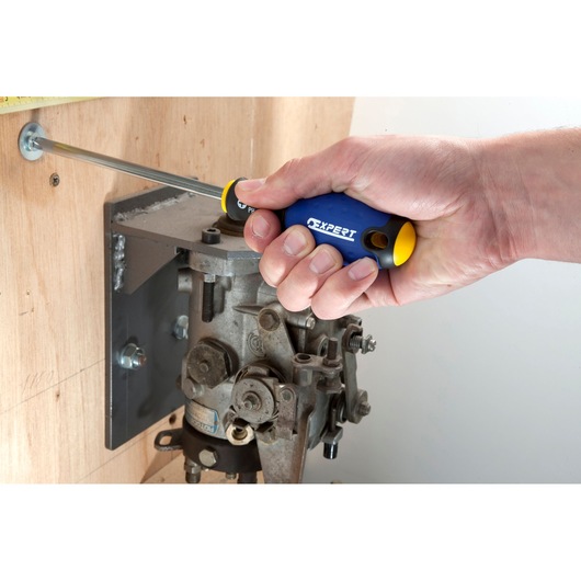 Facom E165206 screwdriver with blue and yellow handle, used to tighten a screw on wood near machinery.