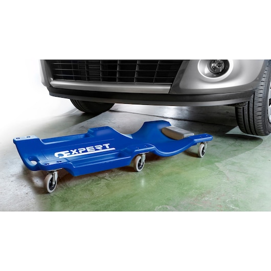Facom E200114 blue mechanic creeper with wheels in garage under car, side angle.