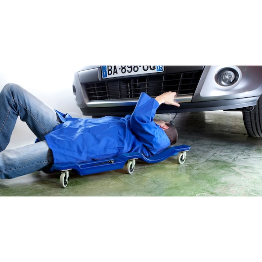 Facom E200114 mechanic on blue creeper working under car, automotive workshop setting.