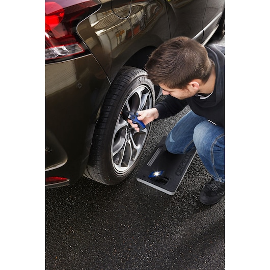 Facom E200131 pad in use with person kneeling beside car wheel, holding a tool, outdoor setting.