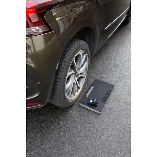Facom E200131 automotive tool case beside car rear wheel on asphalt, top view, photography