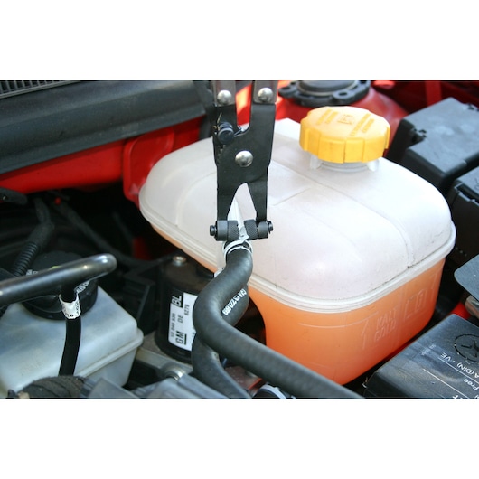 Facom E200504 hose clamp pliers used on a black hose near an orange coolant reservoir in a car engine bay.