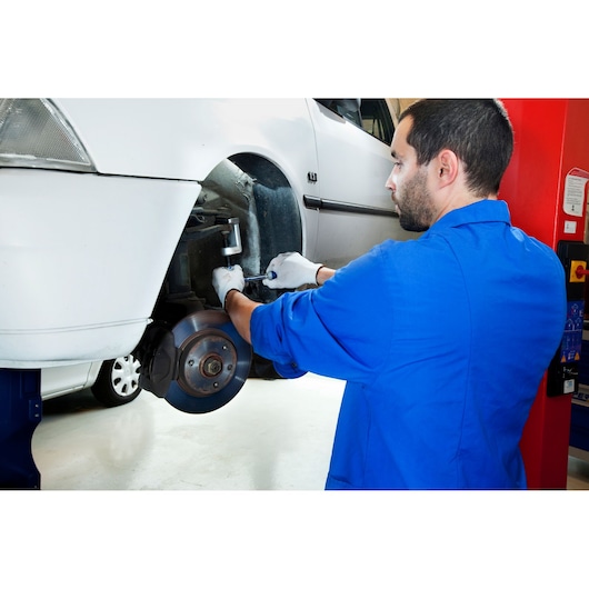 Facom E201100 photography of mechanic in blue coat working on white car brake system in garage.