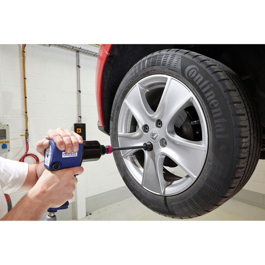 Facom E201131 impact wrench used to remove lug nut from car wheel in garage setting.