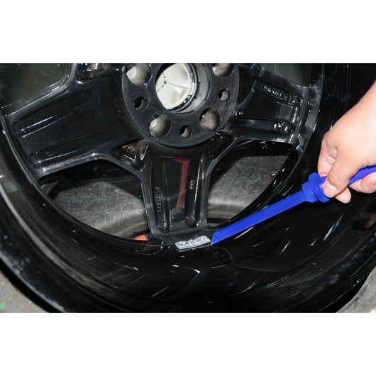 Facom E201204 tool removing wheel balance weight from black alloy wheel, close-up angle.