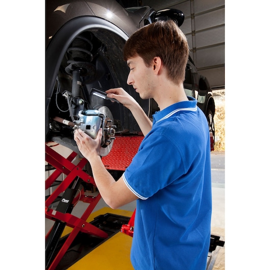 Facom E201406 photography of a person inspecting a car brake assembly in a garage setting.