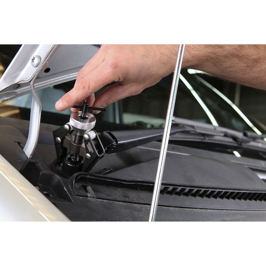 Facom E201512 windshield wiper arm removal tool in use on car, close-up photography.