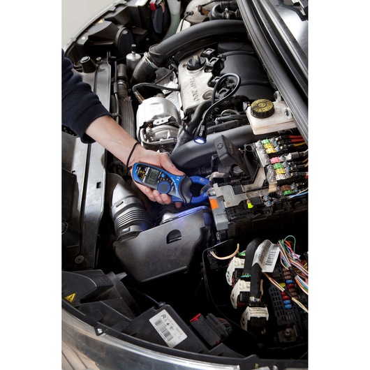 Facom E201803 clamp meter being used to test electrical connections in a car engine bay.