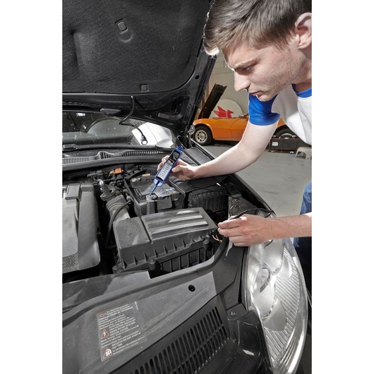 Facom E201804 battery tester used on car battery in garage setting.