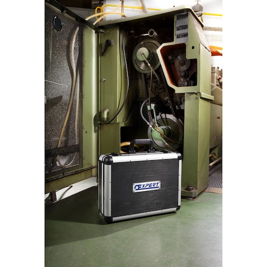 Facom E220109 tool case with black and silver hard shell, Expert logo, placed on workshop floor near industrial machine.